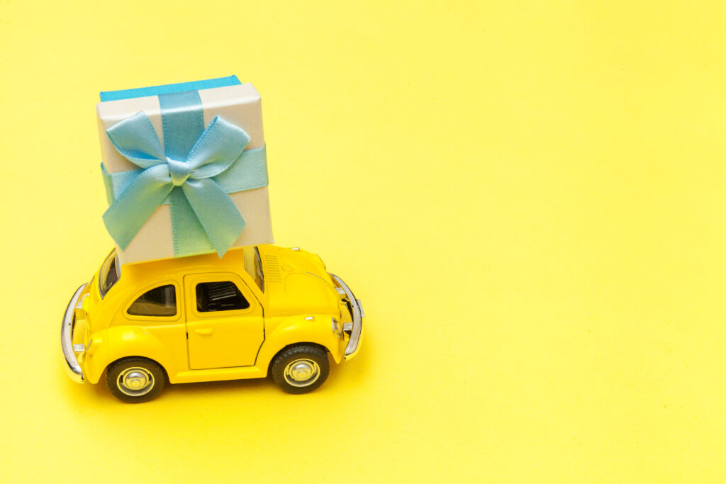 international gift reseller yellow vintage retro toy car delivering gift box on roof yellow background